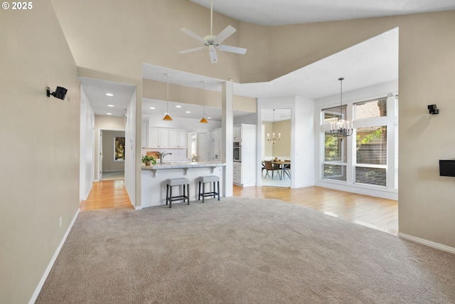 living area featuring light colored carpet, a chandelier, baseboards, ceiling fan, and high vaulted ceiling