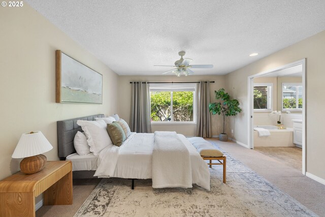 bedroom with carpet flooring, a textured ceiling, ensuite bath, baseboards, and a ceiling fan