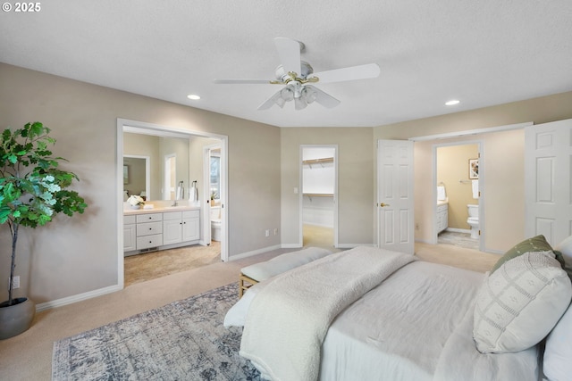 bedroom with light carpet, connected bathroom, baseboards, a walk in closet, and recessed lighting