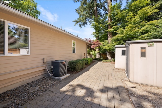 wooden terrace featuring central air condition unit, an outbuilding, a storage shed, fence, and a patio