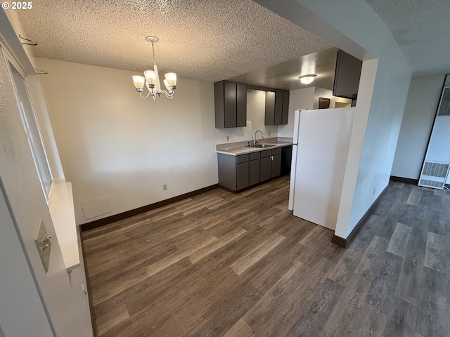 kitchen featuring sink, dark wood-type flooring, a notable chandelier, white fridge, and a textured ceiling