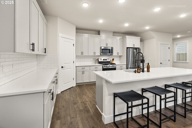 kitchen featuring stainless steel appliances, a center island with sink, a breakfast bar area, and white cabinets