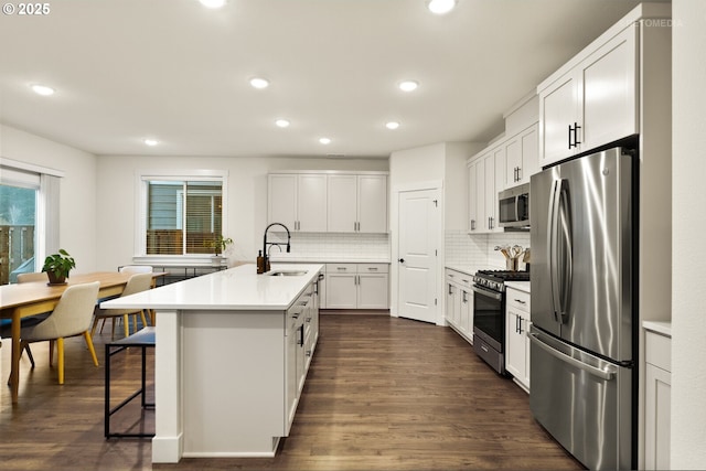 kitchen with a kitchen bar, sink, a center island with sink, stainless steel appliances, and white cabinets