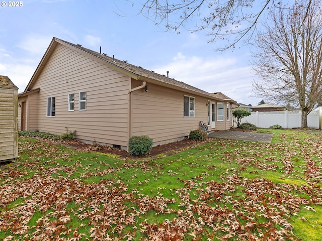 view of side of home featuring a patio, fence, and a lawn