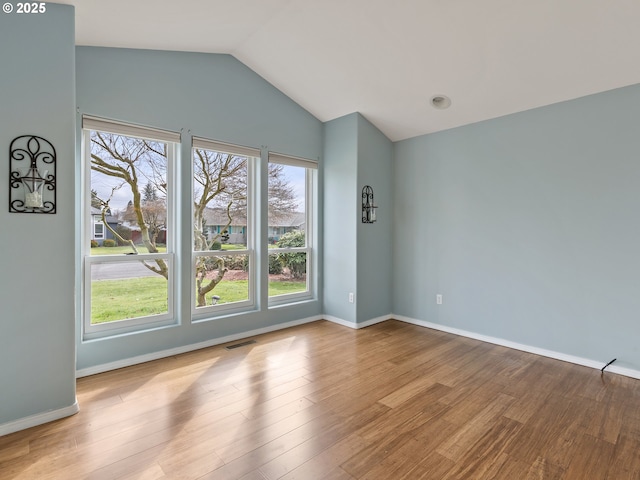 spare room with vaulted ceiling, visible vents, baseboards, and wood finished floors