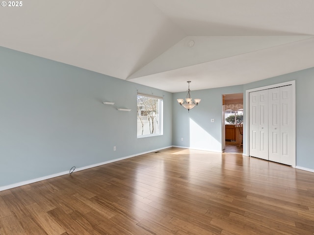 unfurnished room with baseboards, a notable chandelier, wood finished floors, and vaulted ceiling