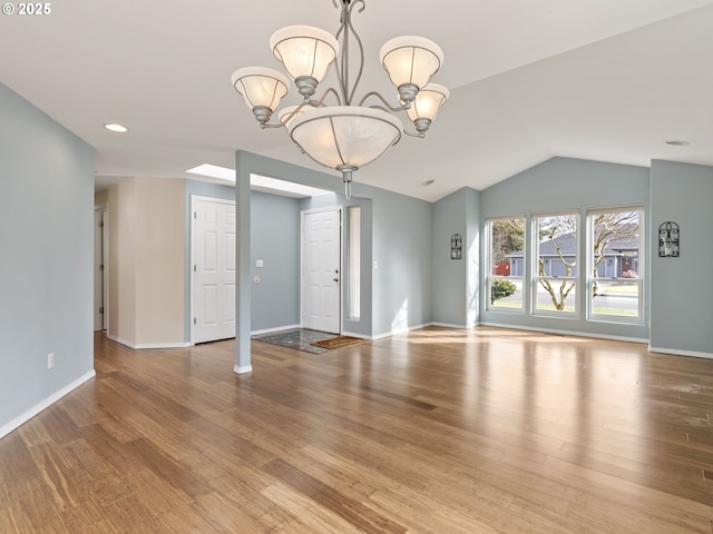 unfurnished living room featuring vaulted ceiling, a notable chandelier, wood finished floors, and baseboards