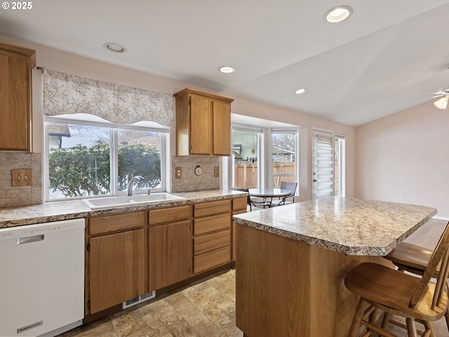 kitchen with visible vents, a kitchen island, a breakfast bar area, white dishwasher, and a sink