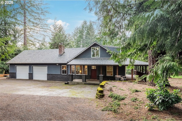 view of front of home featuring brick siding, a chimney, covered porch, a garage, and driveway