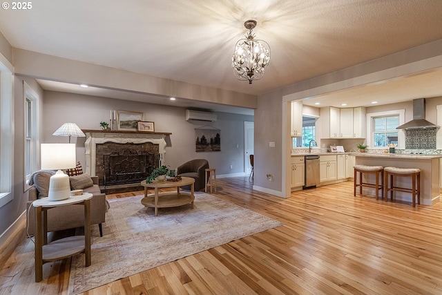 living area featuring light wood-style floors, a fireplace, an inviting chandelier, and a wall mounted AC