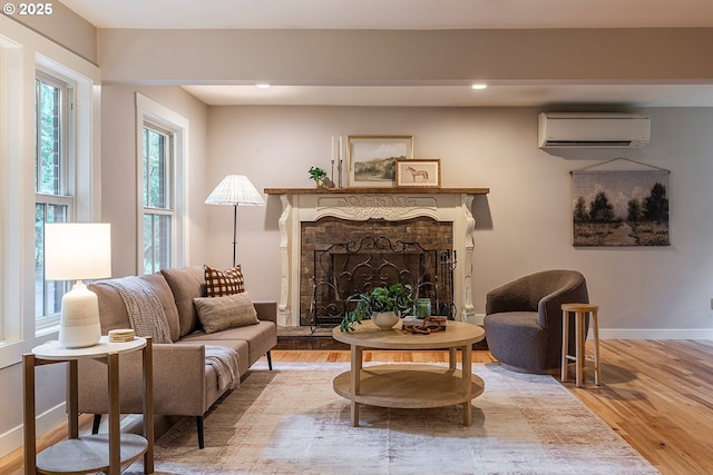 sitting room featuring a fireplace with raised hearth, a wall mounted AC, wood finished floors, and baseboards