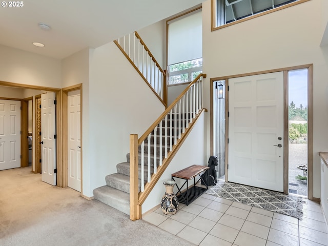 foyer entrance featuring light tile patterned flooring, light colored carpet, a towering ceiling, and stairs