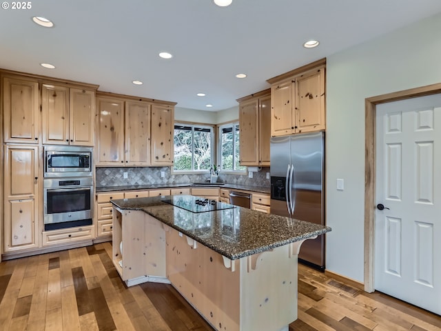 kitchen featuring appliances with stainless steel finishes, dark stone counters, a kitchen island, and a breakfast bar area