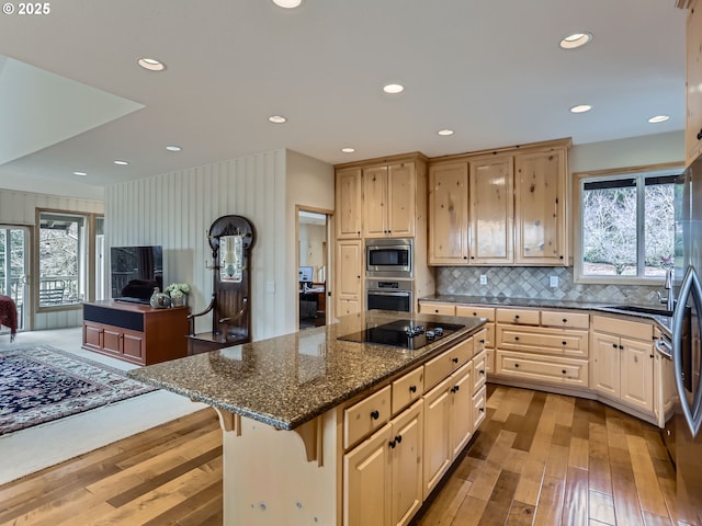 kitchen with a breakfast bar, stainless steel appliances, dark stone counters, a kitchen island, and light wood-type flooring