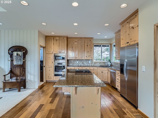 kitchen featuring dark stone counters, a kitchen island, stainless steel appliances, light brown cabinetry, and a sink