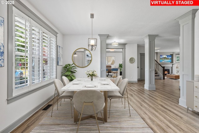 14716 Blue Blossom Way, Oregon City, OR 97045 - dining space featuring decorative columns, light wood-style floors, healthy amount of natural light, and a lit fireplace