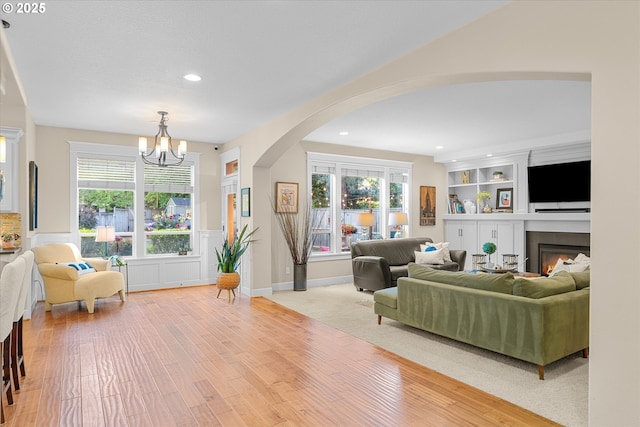 2121 Ostman Rd, West Linn, OR 97068 - living room with arched walkways, a chandelier, light wood-style floors, recessed lighting, and a warm lit fireplace