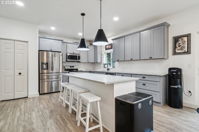 kitchen featuring a kitchen island, a kitchen breakfast bar, stainless steel appliances, light countertops, and pendant lighting