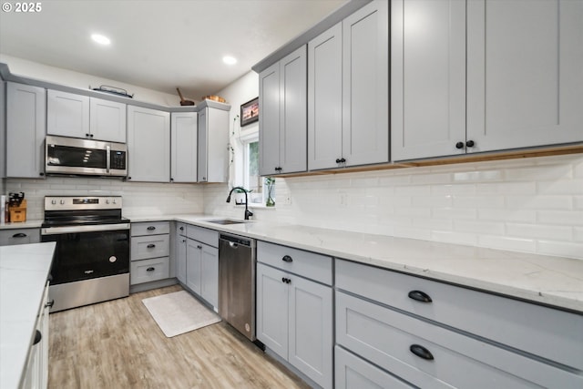 kitchen with light stone countertops, appliances with stainless steel finishes, a sink, and gray cabinetry