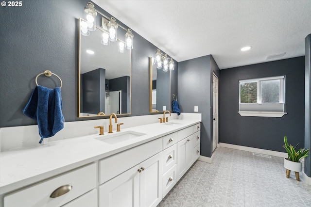 bathroom with a textured ceiling, double vanity, a sink, and baseboards