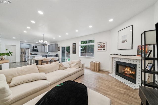 living room with a chandelier, recessed lighting, a fireplace, baseboards, and light wood-style floors