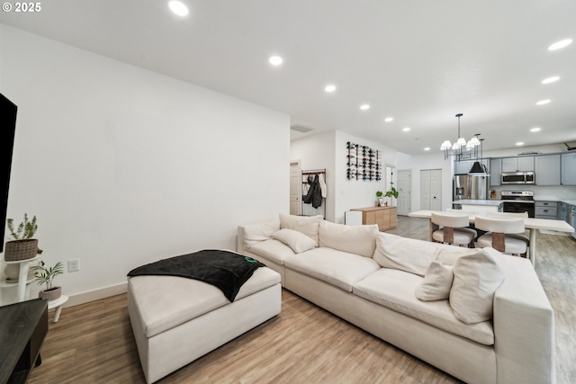 living room featuring light wood-style floors, baseboards, an inviting chandelier, and recessed lighting