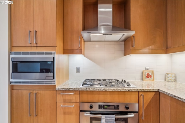 kitchen with wall chimney range hood, light stone counters, tasteful backsplash, and stainless steel appliances