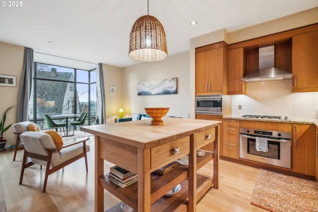 kitchen featuring light wood finished floors, appliances with stainless steel finishes, wall chimney exhaust hood, backsplash, and butcher block counters