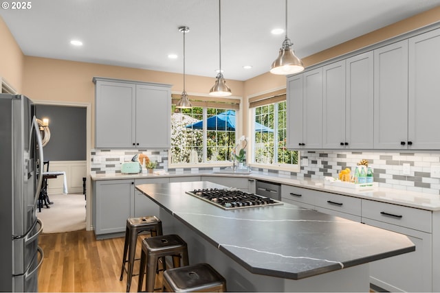 342 NW 84th Pl, Portland, OR 97229 - kitchen featuring stainless steel appliances, a kitchen breakfast bar, light wood-style flooring, decorative backsplash, and hanging light fixtures