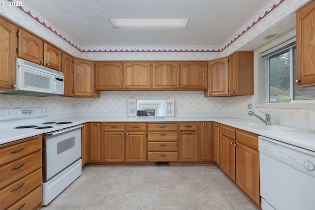 kitchen with white appliances, brown cabinetry, and a sink