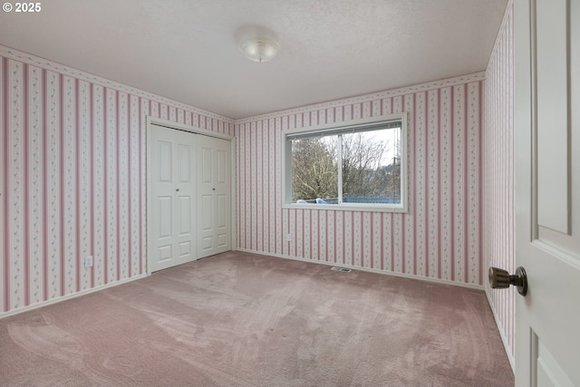 unfurnished bedroom with wallpapered walls, carpet, visible vents, and a closet