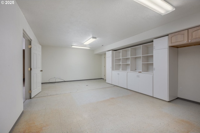 finished below grade area with baseboards, a textured ceiling, and light floors