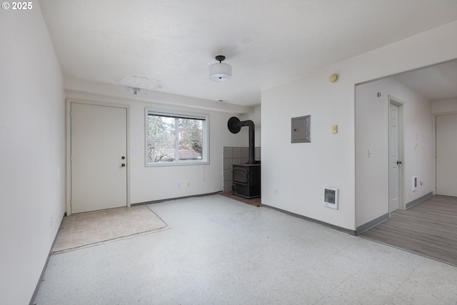 interior space featuring a wood stove, electric panel, baseboards, and tile patterned floors