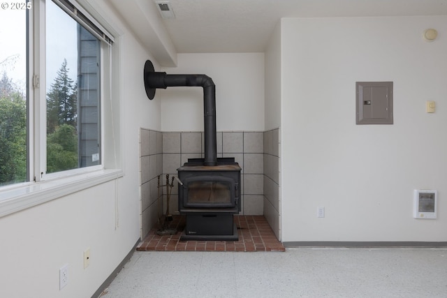 room details with a wood stove, electric panel, visible vents, and baseboards