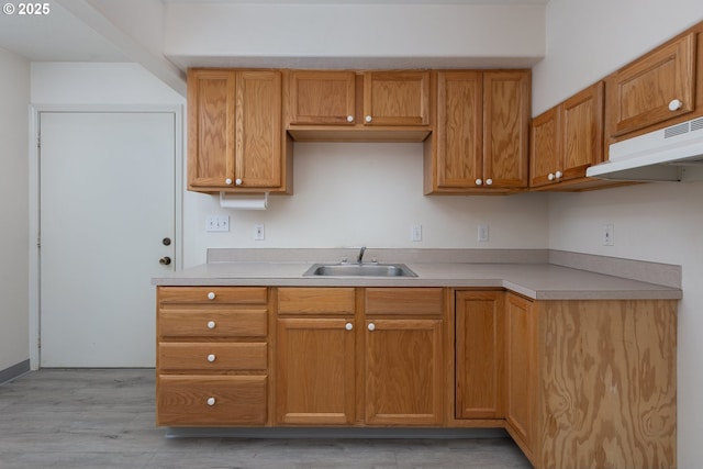 kitchen with light countertops, brown cabinetry, a sink, light wood-type flooring, and under cabinet range hood