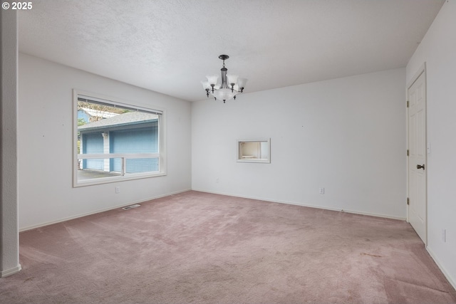 empty room with visible vents, an inviting chandelier, carpet flooring, a textured ceiling, and baseboards