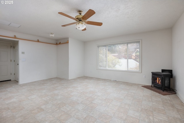 unfurnished living room featuring a wood stove, ceiling fan, baseboards, and a textured ceiling