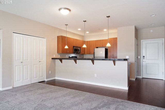 8712 N Decatur St Unit 302, Portland, OR 97203 - kitchen with freestanding refrigerator, stainless steel microwave, brown cabinetry, a kitchen breakfast bar, and recessed lighting