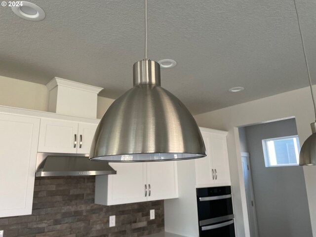 interior details with a textured ceiling, pendant lighting, decorative backsplash, double oven, and white cabinets