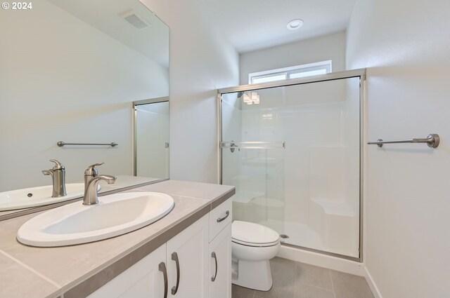 bathroom with a shower with door, vanity, tile patterned floors, and toilet