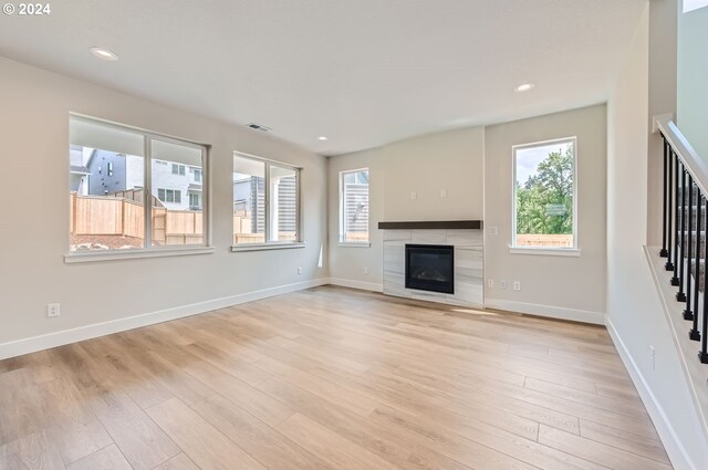 unfurnished living room featuring a tile fireplace, a wealth of natural light, and light hardwood / wood-style flooring