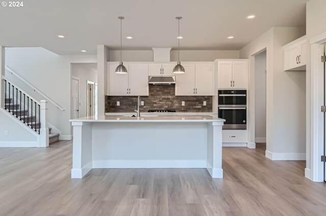 kitchen with decorative light fixtures, an island with sink, light wood-type flooring, white cabinetry, and appliances with stainless steel finishes