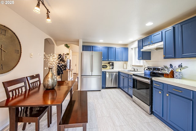 kitchen featuring blue cabinetry, light countertops, under cabinet range hood, appliances with stainless steel finishes, and backsplash