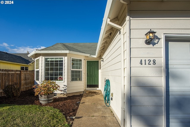 doorway to property with fence and roof with shingles