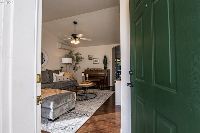 foyer featuring a ceiling fan, a wall mounted AC, dark wood finished floors, arched walkways, and vaulted ceiling