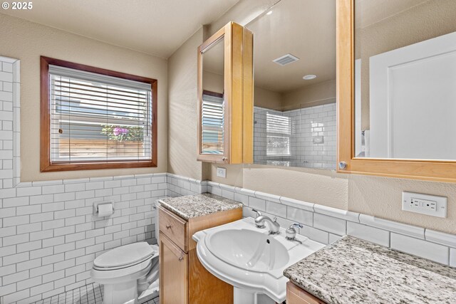 bathroom with tile walls, a sink, toilet, and a wainscoted wall