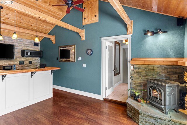 kitchen with wood ceiling, stainless steel microwave, a wood stove, a ceiling fan, and wood finished floors