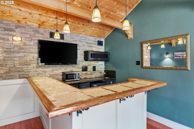 kitchen featuring stainless steel microwave, wood finished floors, wooden ceiling, pendant lighting, and baseboards
