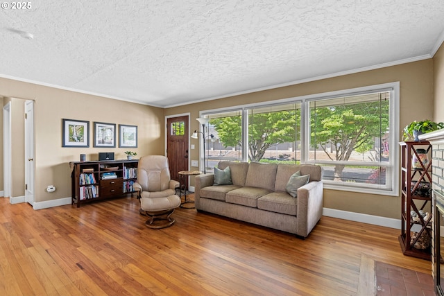 living area featuring a textured ceiling, light wood-style flooring, ornamental molding, and baseboards
