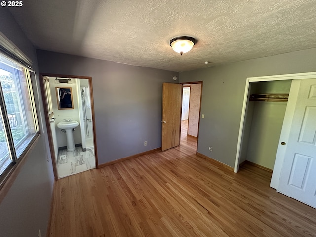unfurnished bedroom featuring wood finished floors, baseboards, a closet, a textured ceiling, and a sink